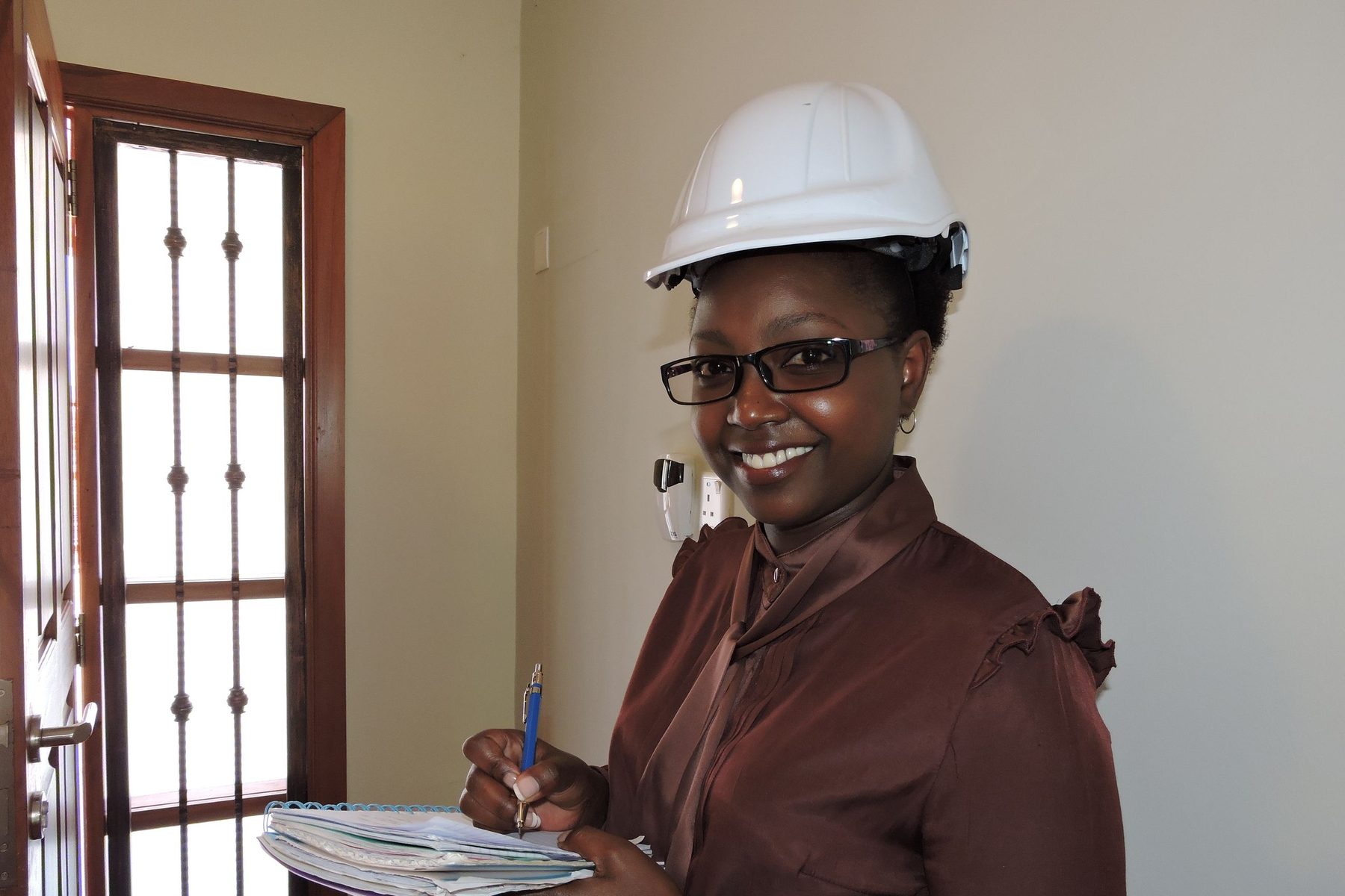 A smiling contractor in a hard hat holding her site paperwork