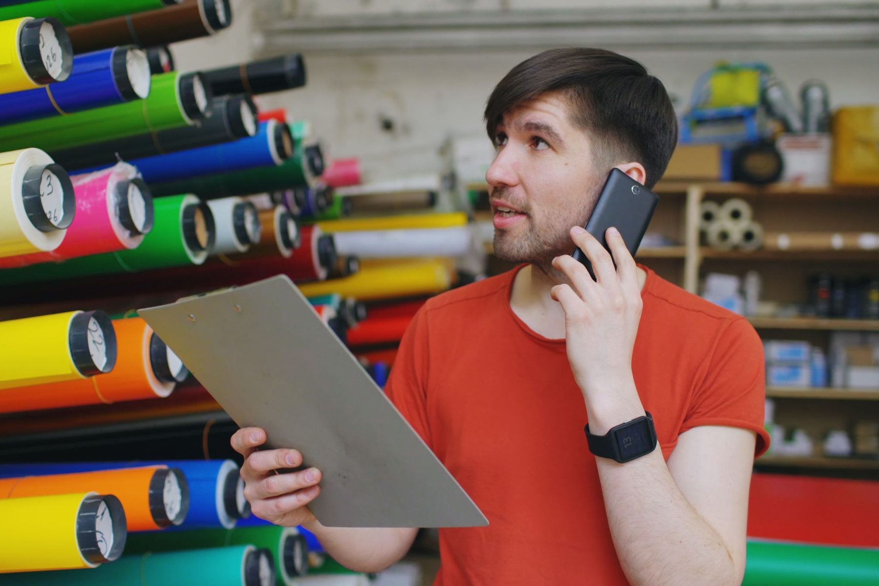 A distribution manager taking a call in his warehouse with a clipboard in hand