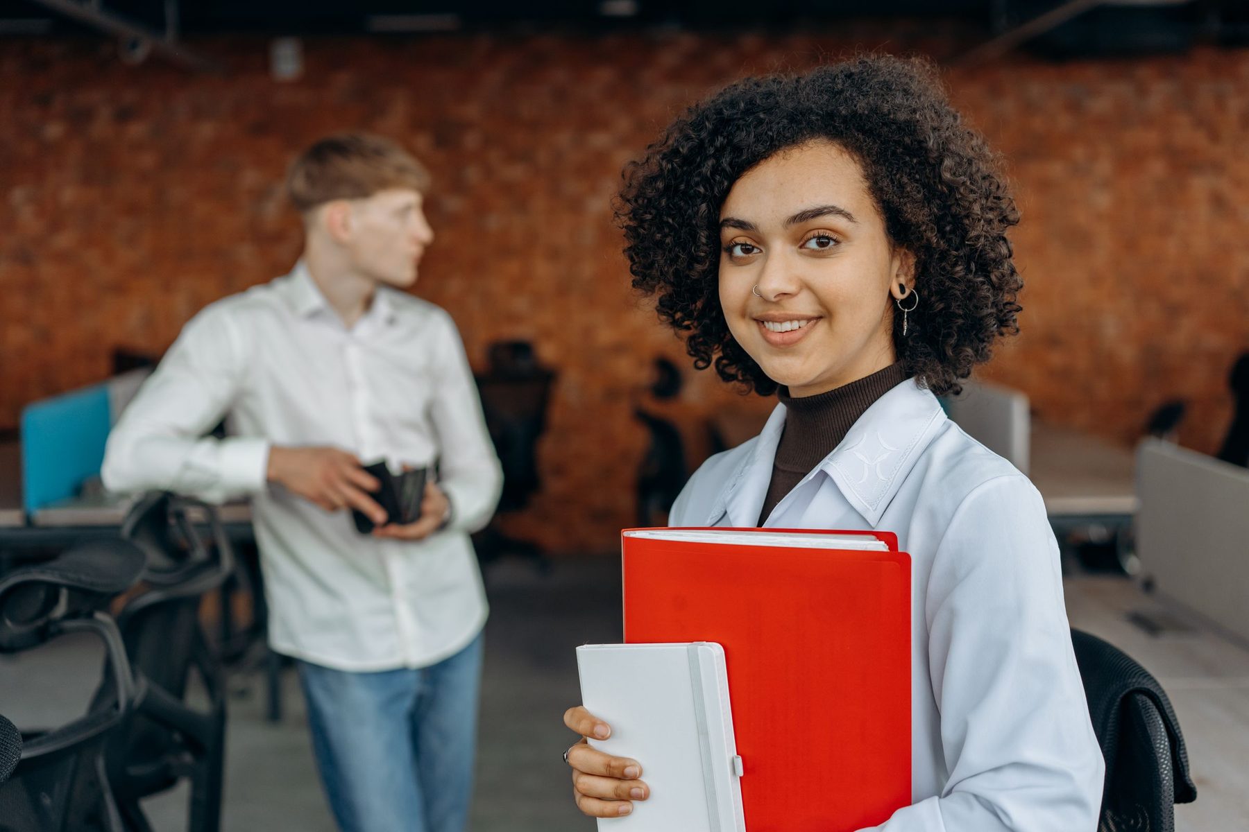 A smiling accountant holding client files and a calculator, with a colleague behind her