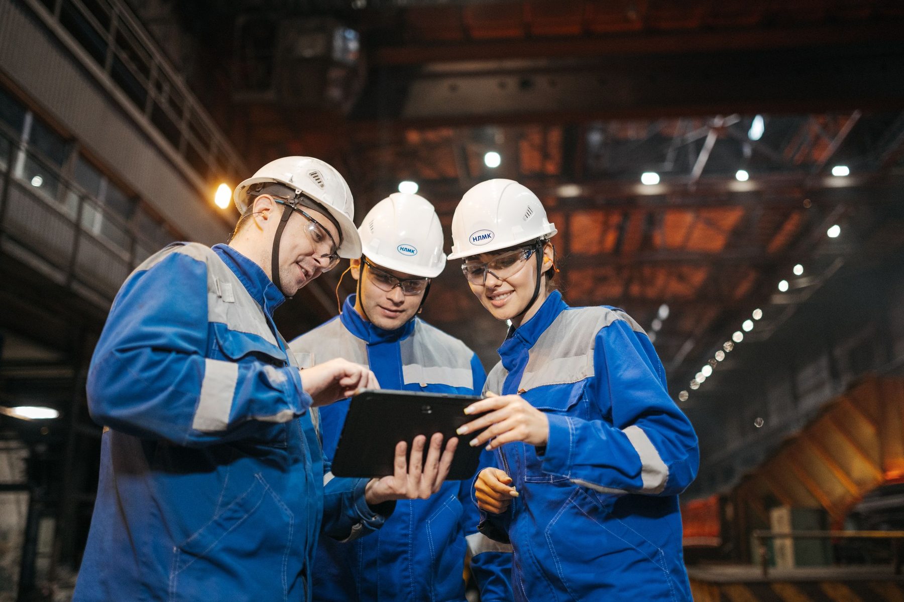 A manufacturing team in work wear checking production numbers on a tablet on the factory floor