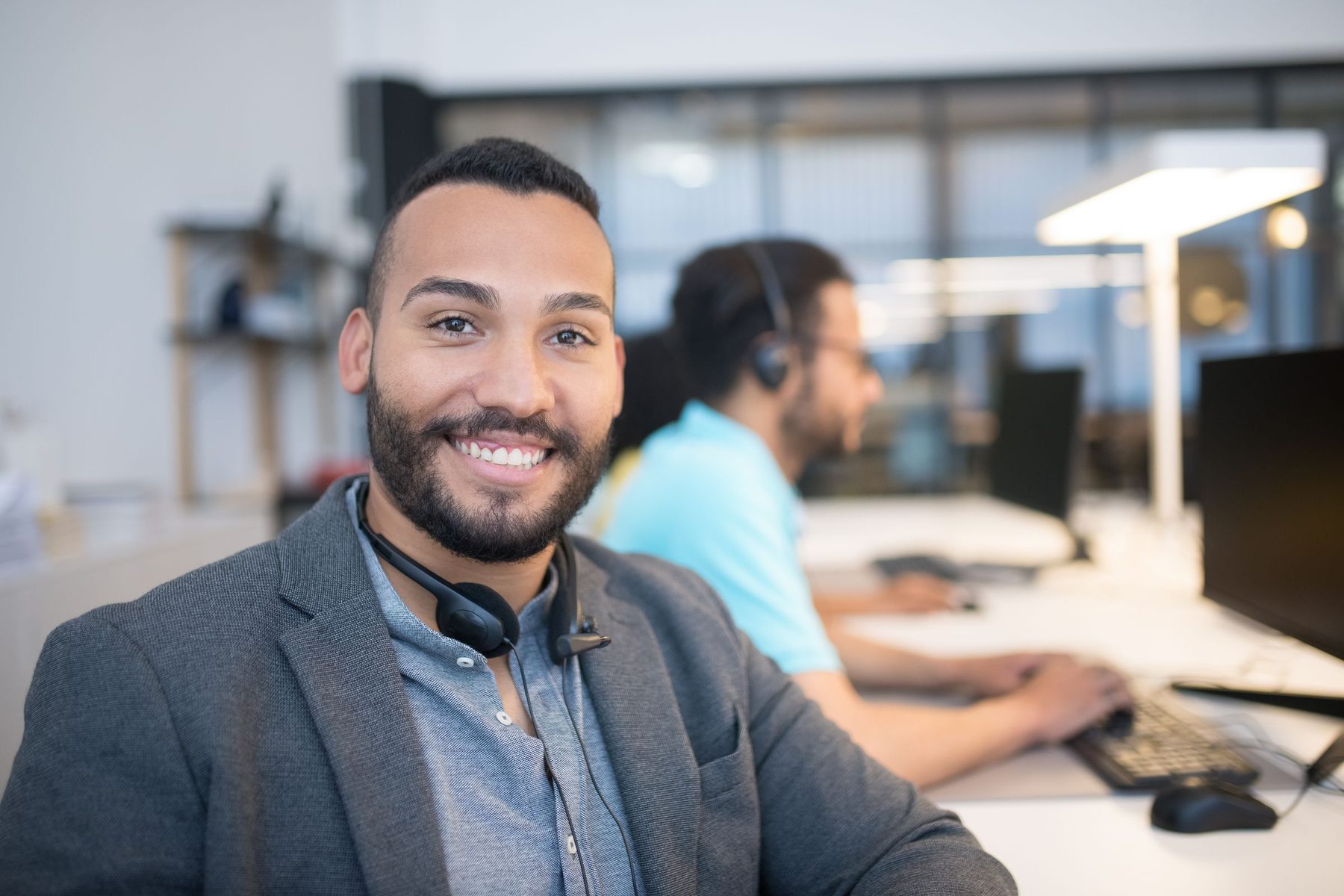 A smiling freight broker with a headset at his desk in a busy logistics office